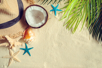 Straw hat, coconut, starfish and shells on white fine sand.