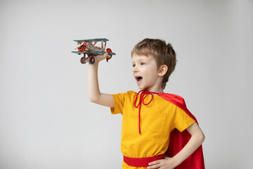 Little superhero boy in a red cape plays with an airplane. Happy smiling child. Success, motivation and travel.