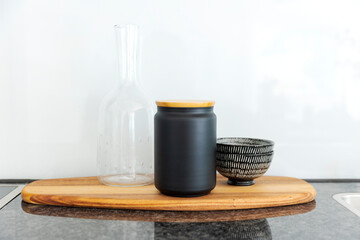 Front view of an elegant wooden tray with a black vase with wooden lid, a glass pitcher and a bowl resting on it. - 782011315