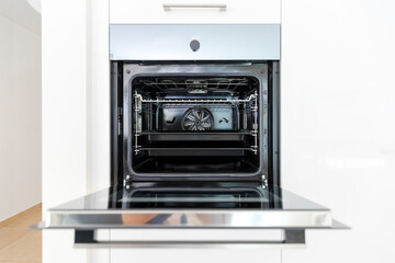 Detail of a new open oven with two baking trays inside. Interior of a modern white kitchen.