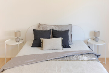 Front detail of a double bed with very large pillows on it and the blankets moved. On the sides there are two comfortable minimalists with bajours on top - 782011354