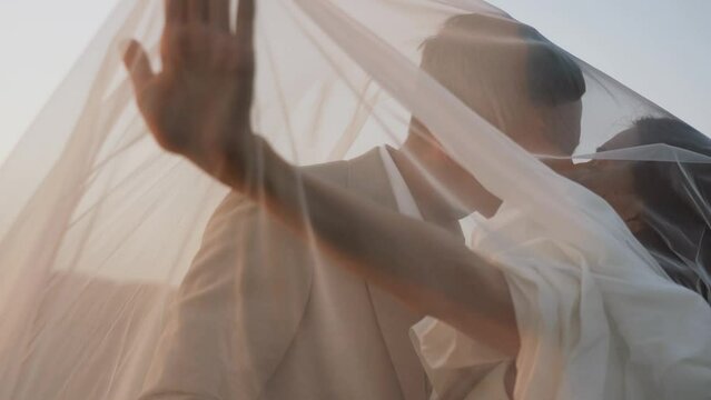 The bride and groom walk at sunset through beautiful fields and hills, laugh and dance. Wedding day concept