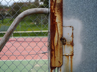 Porte fermé en métal avec rouille et serrure qui donne sur court de tennis