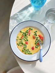 Breakfast omelette with green peas, cherry tomatoes on a plate. Top view. Blue glass of water. Natural light