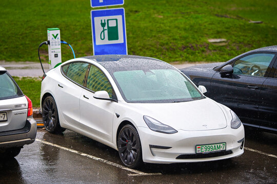 Minsk, Belarus. Apr 6, 2024. Tesla Model 3 charges up battery in rainy day. White Tesla Model 3 parked at charging station. Electric vehicle charging battery at parking lot in wet weather.