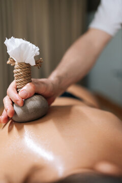 Cropped vertical shot of Ayurveda Massage therapist pressing herbal bolus bags onto female skin. Masseur gently compresses herb bag on woman body. Hot herbal ball spa massage body treatment.