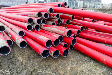 A pile of red pipes are stacked on top of each other. The pipes are made of plastic and are red in...