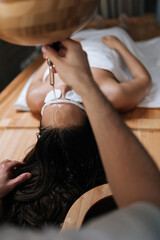 Vertical shot of shirodhara essential oil poured on forehead of young relaxed woman with cotton...