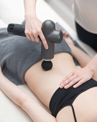 Massaging girl's back with massage gun. massage therapist holds shock vibration electric massager in hand. Massage with shock electric massager for pain in back muscles. Vibration therapy. Side view.