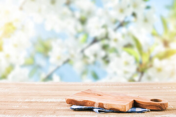 Empty rustic wooden table with blue tablecloth and wooden board over rapeseed blooming summer garden on sunny day background. Harvest mock up for design.