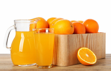 Fresh oranges in crate and juice on wooden table against white background