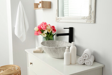 Fototapeta na wymiar Vase with beautiful pink tulips and toiletries near sink in bathroom