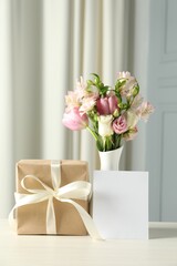 Happy Mother's Day. Gift box, blank card and bouquet of beautiful flowers in vase on white table indoors