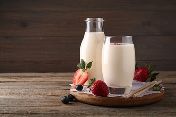 Tasty yogurt in glass, bottle, straws and berries on wooden table. Space for text