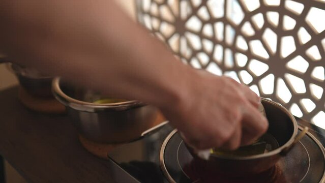 Cropped shot of ayurvedic massage practitioner dipping cotton-wrapped herbal bundle into aromatic oil during prepare to Shirodhara treatment. Tranquil and serenity of aromatherapy recreation at salon.
