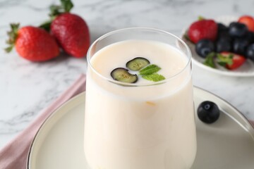 Tasty yogurt in glass and berries on white table, closeup