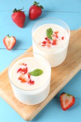 Tasty yogurt in glasses and strawberries on light blue wooden table