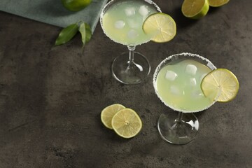 Delicious Margarita cocktail with ice cubes in glasses and limes on grey table, space for text