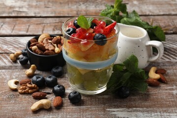 Delicious fruit salad, fresh berries, mint and nuts on wooden table