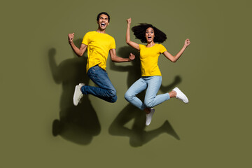 Full size photo of two young people jump raise fists wear t-shirt isolated on khaki color background