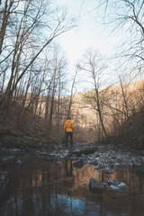 Young man in an orange jacket relaxes in the flow of a river in the Wallonia region of Belgium. Reflection of a man in the river water. Discovering wildlife in Belgium