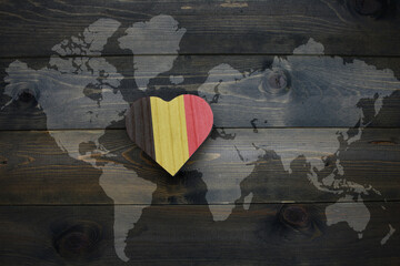 wooden heart with national flag of belgium near world map on the wooden background.