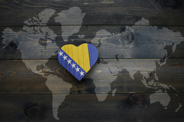 wooden heart with national flag of bosnia and herzegovina near world map on the wooden background. - obrazy, fototapety, plakaty