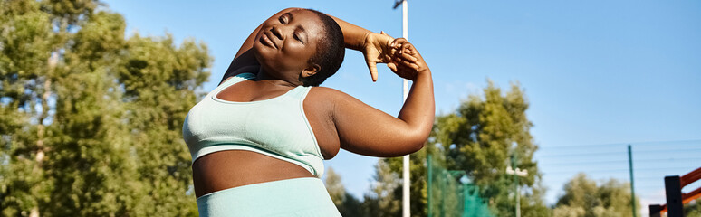 An African American woman in sportswear confidently stretching her arms outdoors, embracing her body positivity.