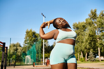 A curvy African American woman in sportswear confidently stretching her arms outdoors, exuding strength and determination.
