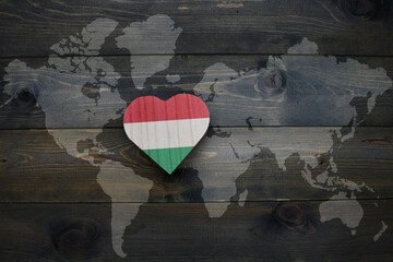 wooden heart with national flag of hungary near world map on the wooden background.