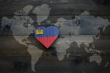 wooden heart with national flag of liechtenstein near world map on the wooden background. - obrazy, fototapety, plakaty
