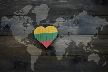 wooden heart with national flag of lithuania near world map on the wooden background.
