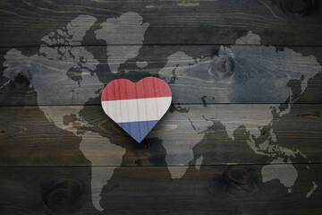 wooden heart with national flag of netherlands near world map on the wooden background.