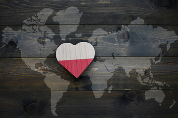 wooden heart with national flag of poland near world map on the wooden background.