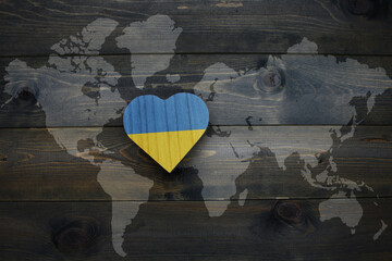 wooden heart with national flag of ukraine near world map on the wooden background.