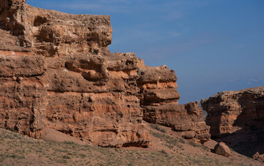 large rock formation against a deep blue sky. The rock's surface is rugged and pitted, with shades of brown that suggest erosion from environmental elements.