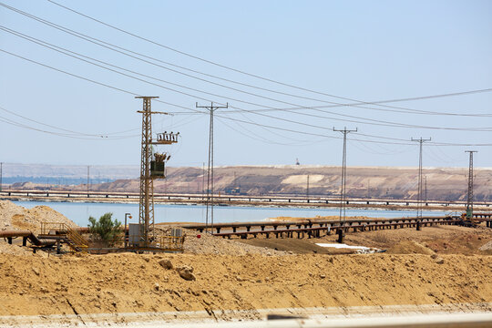 Tranquil afternoon by a serene Dead sea with electrical lines. A peaceful scene unfolds by a calm sea under a clear sky, with utility poles and electrical lines running parallel to the water. Israel