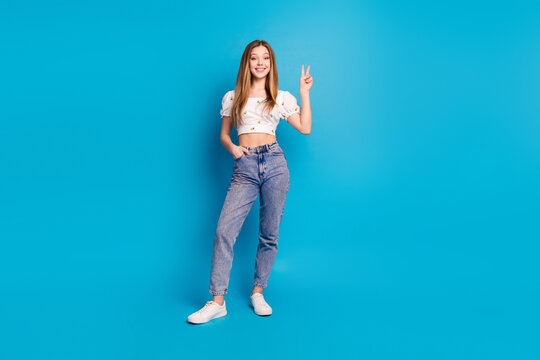 Fototapeta Photo of positive girl stand make v sign isolated blue color background