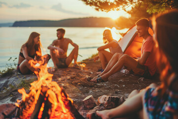 Group of happy friends spending time together camping by the lake, outdoors. Sunset, smiling people sitting by the bonfire. Summertime activities with friends and family creative background. 