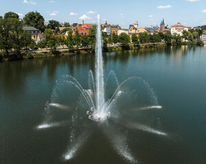 Fountain in the large pond in Altenburg. Summer day in small town in Thuringia. Reflections on the water. Full height fountain. - obrazy, fototapety, plakaty