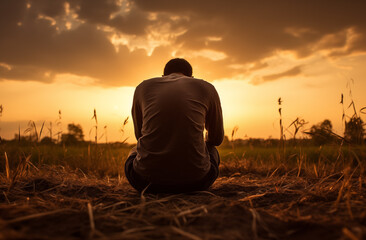Prayer concept. Silhouette of a handsome man in a praying pose. Set against a vibrant sunset sunrise sky. Clasped hands. Also related to anointing, Pentecost, sacrament, authority, kingdom