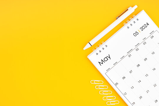 May 2024, Monthly desk calendar for 2024 year and pen with paper clips on yellow color background.