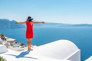 Woman in red dress on the roof enjoying view of Santorini island and Caldera in Aegean sea. Greece.