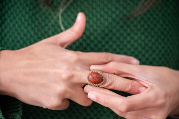 detail of a woman's hands putting on a ring with a stone and woven fabric