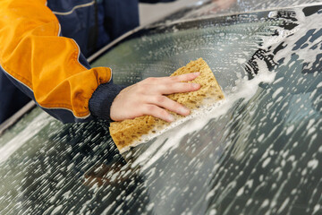 A car wash worker washes a car's windshield using a sponge and car cosmetics