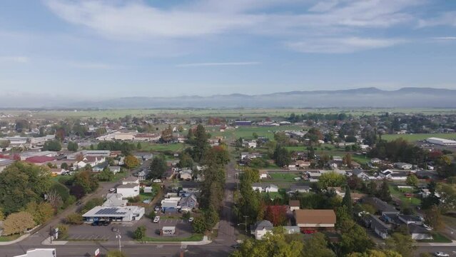 Aerial drone shot of small neighborhood town in Oregon with green hills, mountains, and clouds.