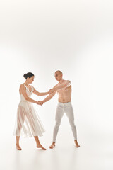 A young shirtless man and a young woman in a white dress dance together, executing acrobatic elements in a studio setting on a white background.