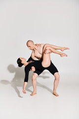 Shirtless young man and dancing young woman perform acrobatic pose in perfect harmony against a white backdrop.