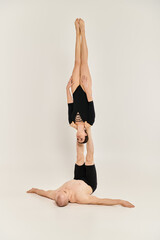 A shirtless young man and a woman performing acrobatic element in perfect synchronicity against a...