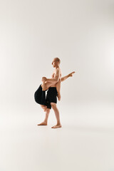 A shirtless young man lifts a woman in black on a white background.